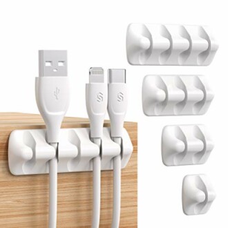 White cable organizer clips attached to a wooden surface, holding USB and charging cables.