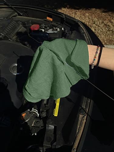 Person checking car oil with green cloth