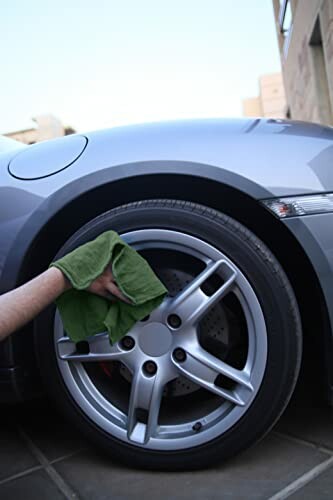 Person cleaning a car wheel with a green cloth