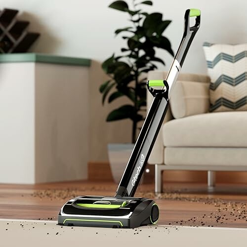 Cordless vacuum cleaner on a wooden floor near a couch and plant.