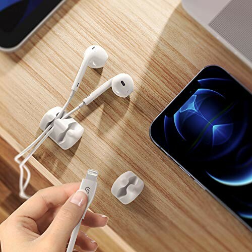 Earphones and cable clips on a wooden desk near a smartphone.