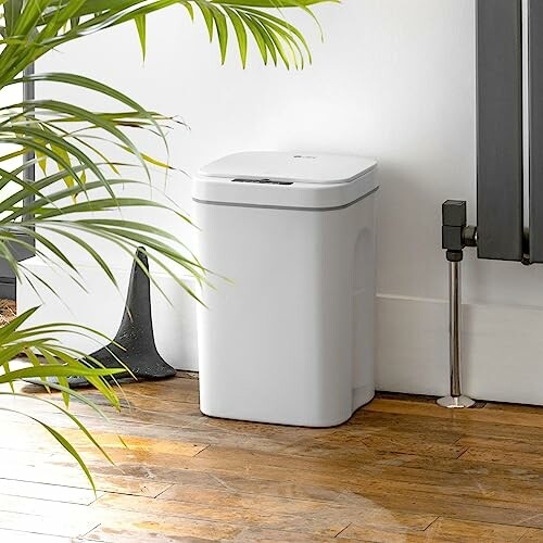 White trash can in a modern kitchen setting with wooden floor and plants.