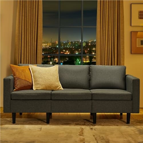 Modern grey sofa with pillows in front of a window overlooking a cityscape at night.