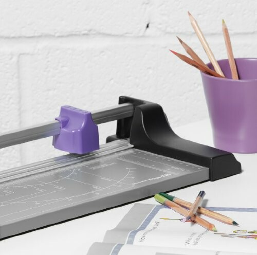 Paper cutter and pencils in a cup on a desk.