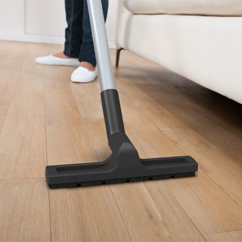 Person vacuuming a wooden floor near a couch