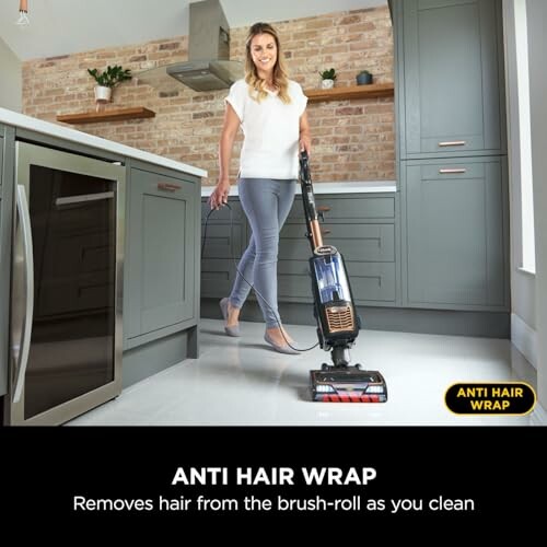 Woman using vacuum cleaner with anti hair wrap feature in a modern kitchen.